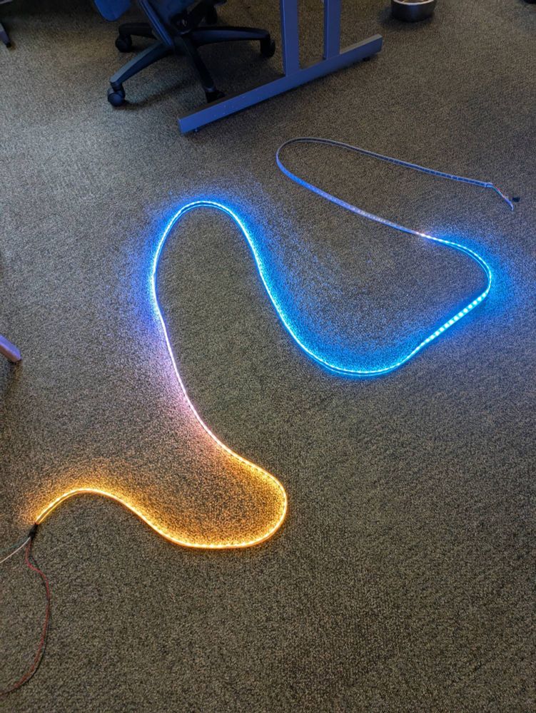 A photo of a strip of coloured LED lights snaked around on a grey carpet. The first LEDs at the top are off and then the LEDs go from blue to orange as they go down.
