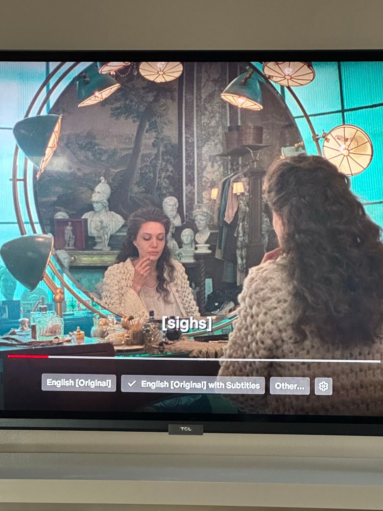 Actress Angelina Jolie in her role as Maria Callas sitting in front a large round mirror rimmed with antique flood lights.