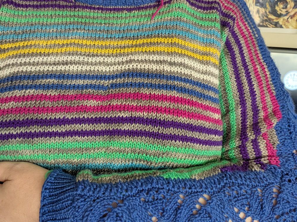 Closeup on hand knit sweater with blue lace panel sleeves and stripes like tv color bars.