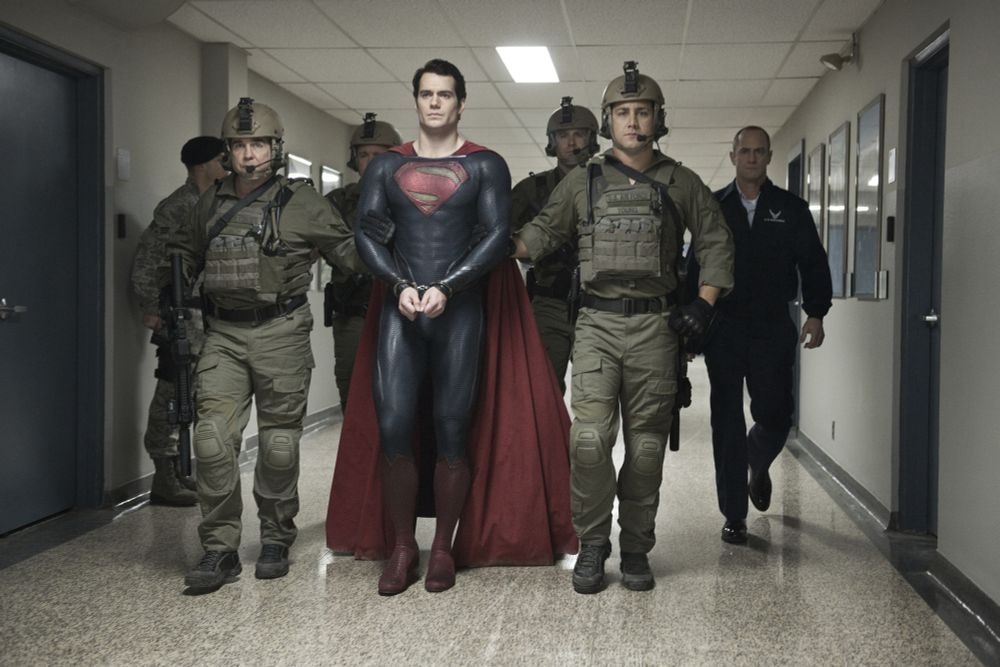 Superman in cuffs being escorted by 4 military men and Elliot Stabler 
