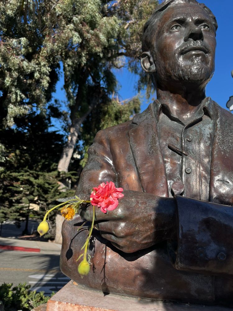 A statue with crossed arms and someone has put a few picked flowers in the statue’s hand
