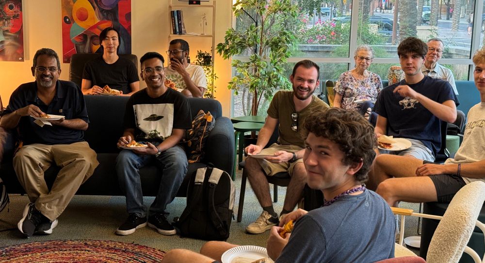 A group of young and old students smiling while eating pizza