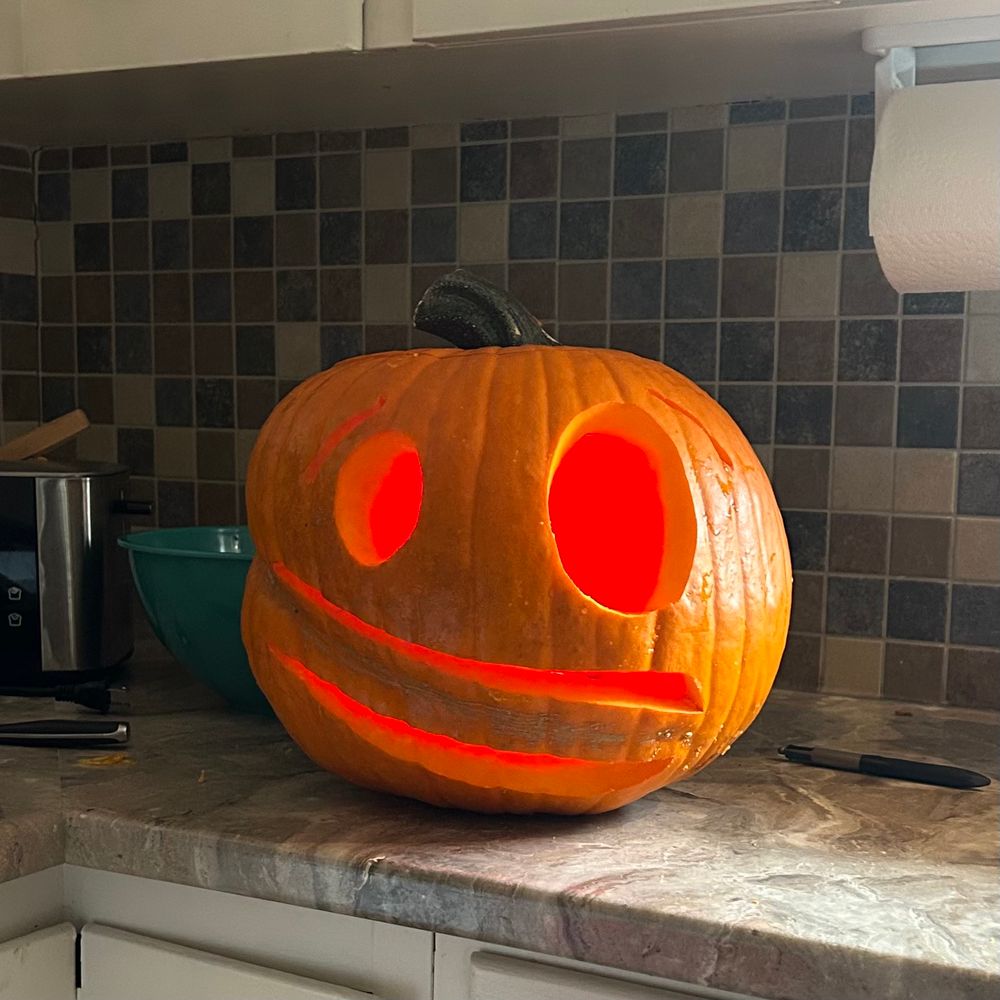 A carved pumpkin with lopsided grin and round eyes sits on a kitchen counter. 