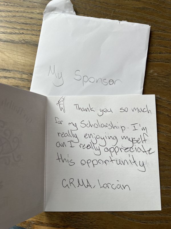 An envelope addressed to “my sponsor” with an open card that says “Thank you so much for my scholarship. I’m really enjoying myself and I appreciate this opportunity. GRMA Lorcain.”