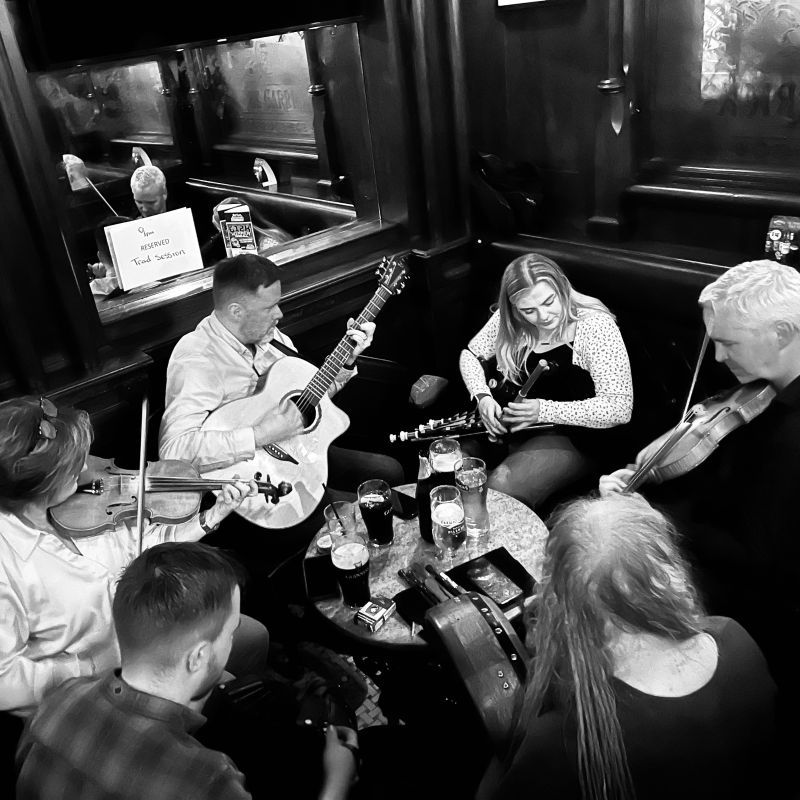 A circle of musicians in a pub corner; fiddles, pipes, and guitar.