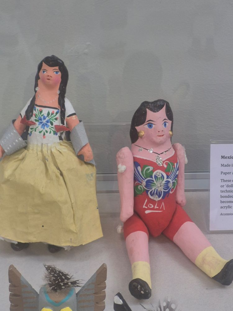 Two dolls in a display case, the first one is wearing a yellow dress and has a pony tails. The second has a red dress with the name Lola on the front. 
