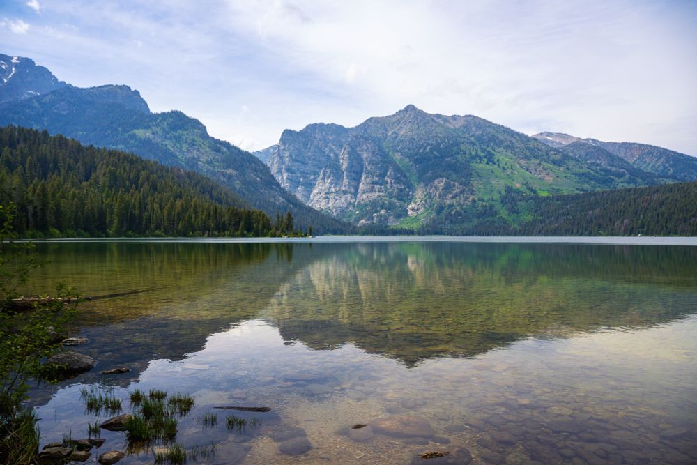 Mountains and pine trees reflect in a crystal clear high mountain lake in Grand Teton National Park. 