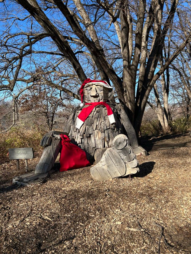 A large wooden troll sitting in front of a tree