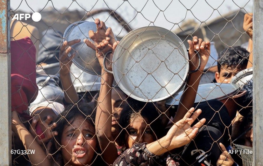 Palestinians push to receive a hot meal at a charity kitchen in Khan Yunis, southern Gaza Strip, on July 22, 2025