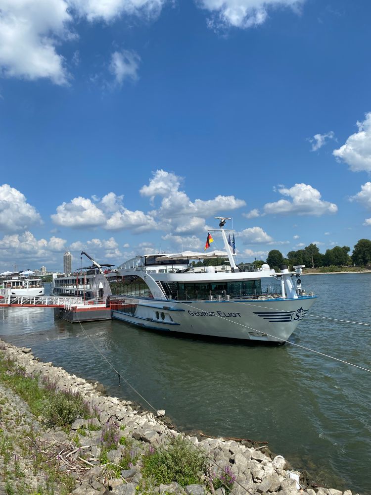 Am Kölner Rheinufer vor Anker liegende Kreuzfahrtschiffe. Blauer Himmel, weiße Wolken.