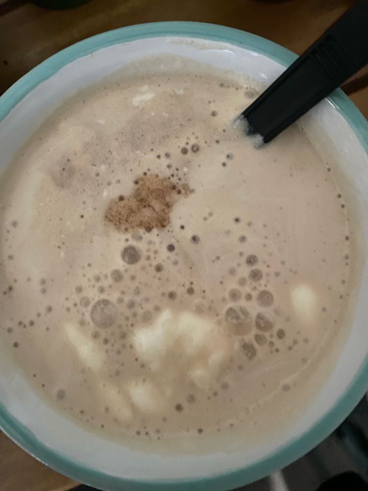 frothy coffee in a blue and white mug with a black spoon 