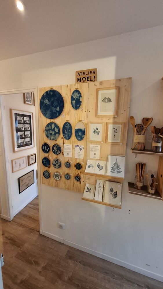 Photo présentant mon nouvel espace de vente. Les créations sont accrochées au mur sur un fond en bois. On y voit des cyanotypes sur tissu montés sur des tambours à broder et des estampes végétales directement imprimées à partir de feuilles 🍃 