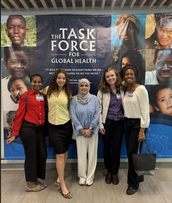 Five students stand in front of a banner with The Task Force for Global Health logo with faces of global health.