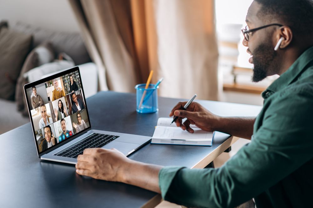 Male African American employee looks at laptop screen with diverse business people meeting online.