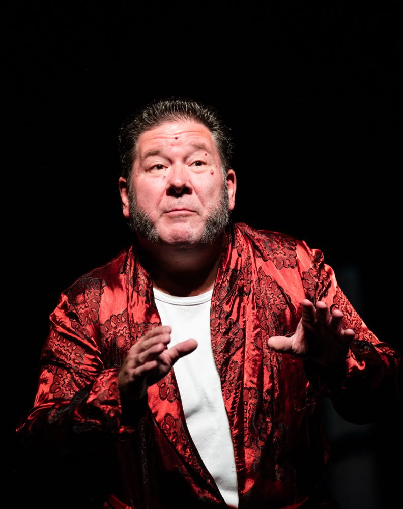 Giffnock Theatre Players - The Matchmaker.
Close image of one of the main characters wearing a white tshirt with a red silk robe. He gestures towards the audience while explaining his big plans. The Matchmaker is a 1954 Broadway play by Thornton Wilder, a rewritten version of his 1938 play The Merchant of Yonkers.
