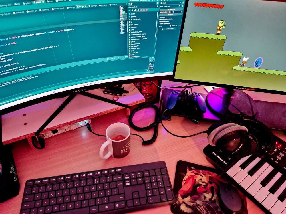A picture of my setup with a cofee and godot and my game are opened on my computer. Some devices can be seen like a sound card, a midi keyboard, a keyboard, a mouse and headphones.