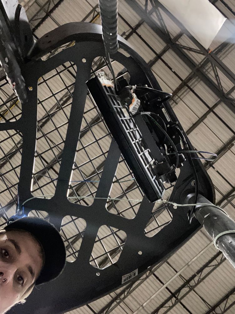 photo of a girl with blonde hair and piercings wearing a hat looking down at the camera while standing in the cab of a forklift