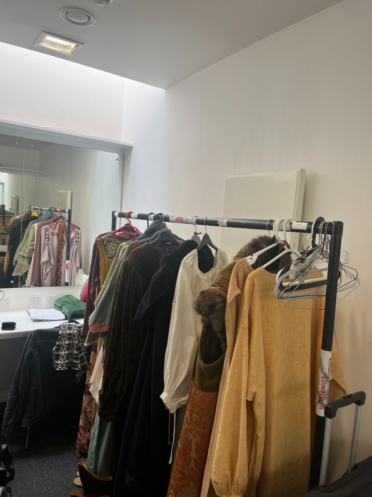 A clothes rack with Shakespearean costumes inside a dressing room.