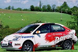 2002 rally Toyota Prius in red and white. The livery says Prius in white on the back, Panasonic in blue on the front. It whips. 
