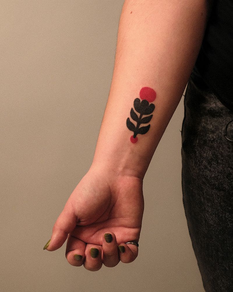 handpoke tattoo on wrist of geometric tulip like flower with 1 big red circle on top and small red circle below. 