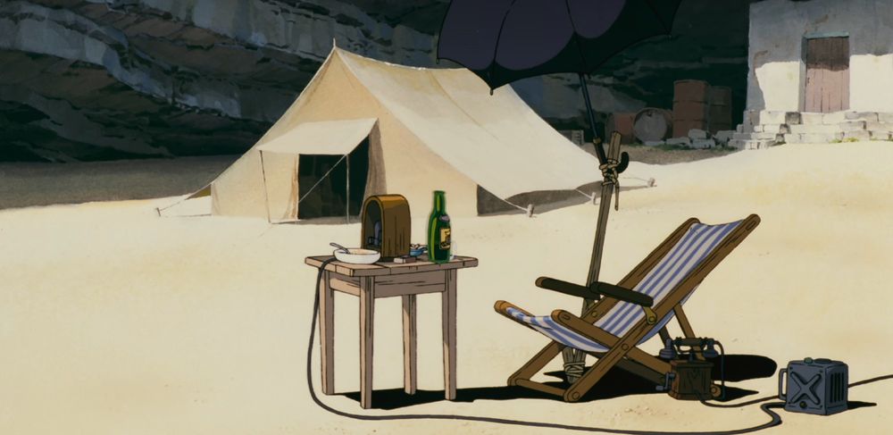 A frame from Porco Rosso (1992) depicting the titular character's hidden island hideout, with a reclining beach chair, parasol, radio, and bottle of wine.