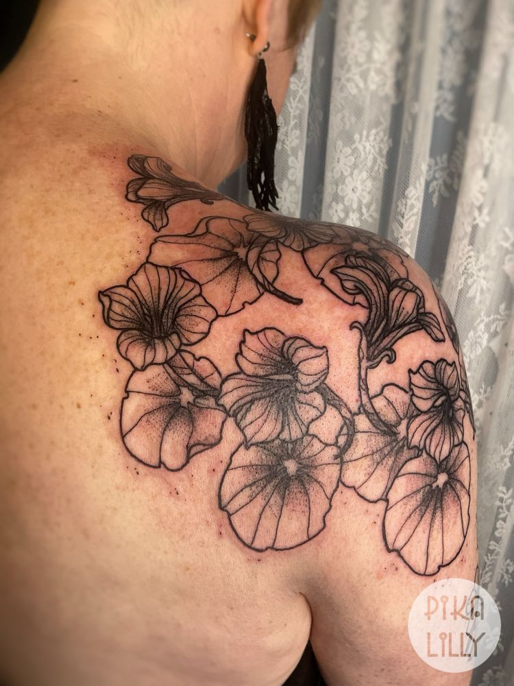 Tatouage en noir de capucines stylisées sur l’épaule et l’omoplate