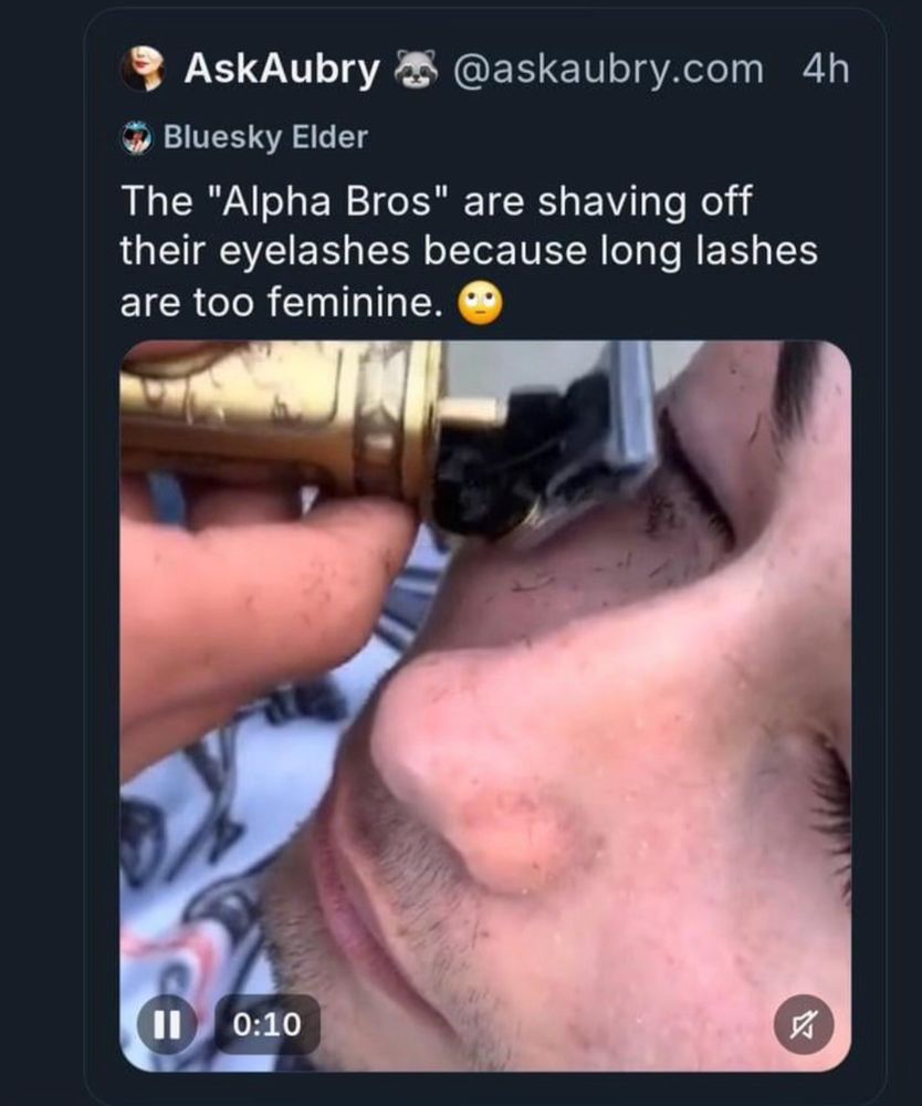 The image is a screenshot of a tweet. The tweet includes a video still showing a close-up of a man having his eyelashes shaved off with a gold-colored electric razor. The text of the tweet reads:
“The ‘Alpha Bros’ are shaving off their eyelashes because long lashes are too feminine.”
The tweet also includes an eye-roll emoji at the end, indicating sarcasm or disbelief.