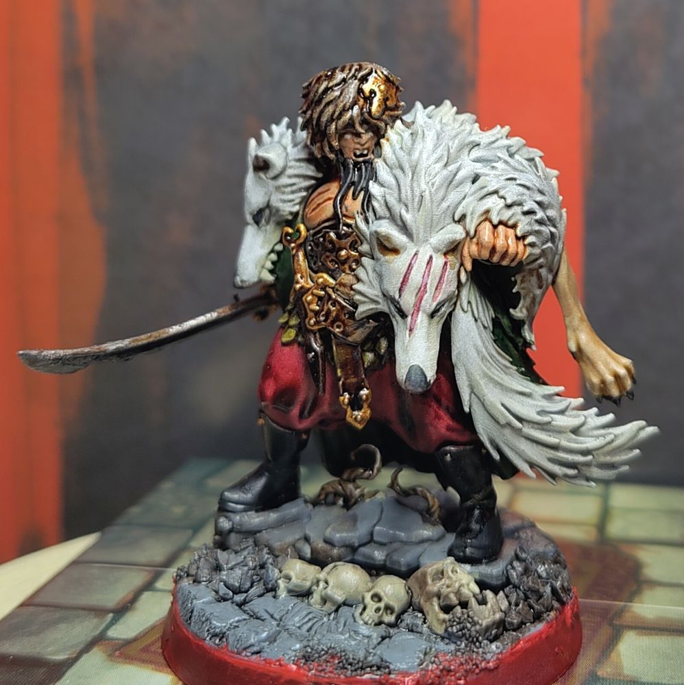 Warhammer Quest Cursed City miniature of Radukar the Wolf, a gargantuan vampire lord barbarian wearing a ushanka, a green greatcloak, and red trousers, with a monstrous two headed wolf pelt across his shoulders. Holding a wicked looking sword and fist extended and fangs bared.