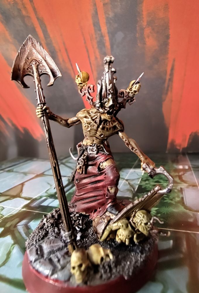 A painted miniature from Warhammer Quest Cursed City of a monstrous figure with a mask of coffin wood and a bare chest, an eight foot tall shovel and hooks, tearing up the floor and exhuming a zombie