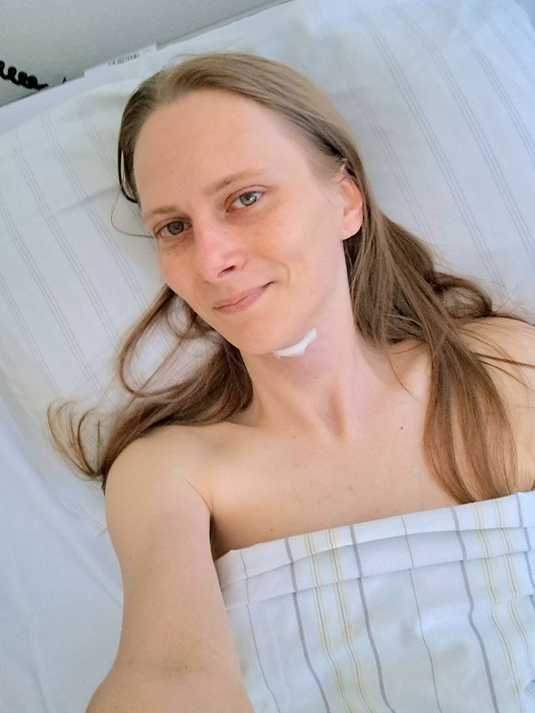 Selfie von Steph. Eine junge blonde Frau liegt in einem Bett. An ihrem Hals ist ein Pflaster zu sehen.