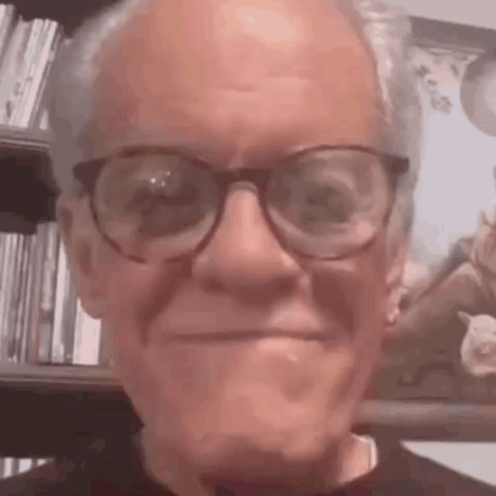 an elderly man wearing glasses is making a funny face in front of a picture .