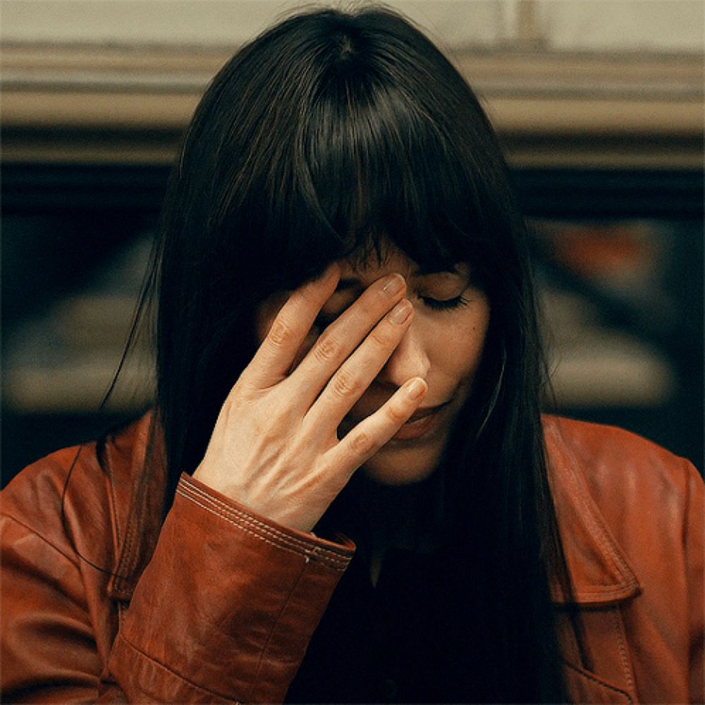 a woman covering her face with her hand while wearing a red leather jacket