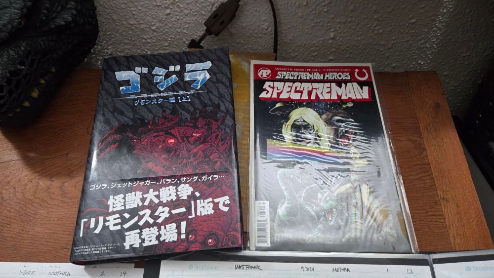 On a drafting table sits a copy of Godzilla rulers of earth reminder edition japan exclusive and a copy of specterman heros. 