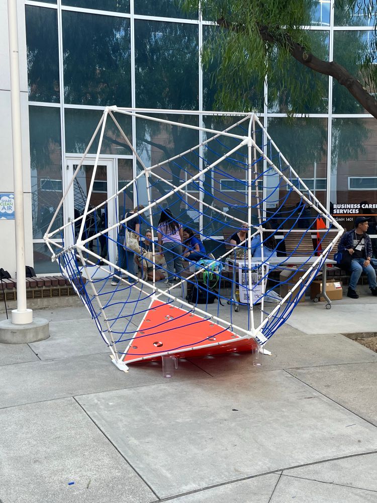 An icosahedral frame built out of PVC pipes, decorated with blue tubes and orange panels to imitate the MAA logo