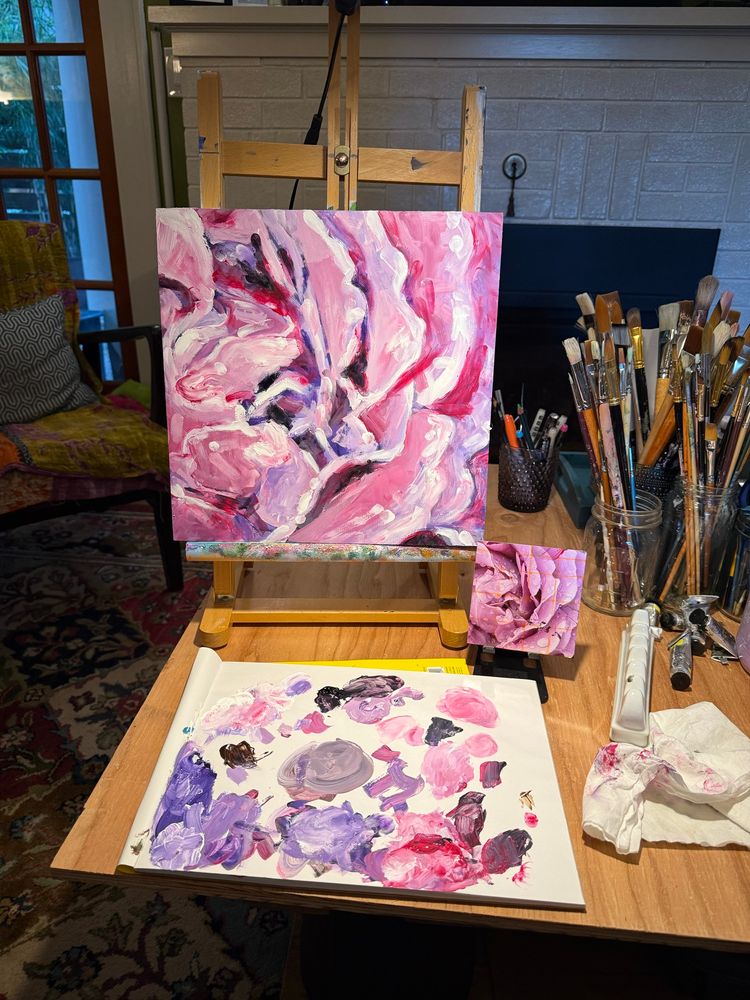 Pic of painting  of a rose in pinks and purples on table easel + palette+ brushes + reference photo. 
