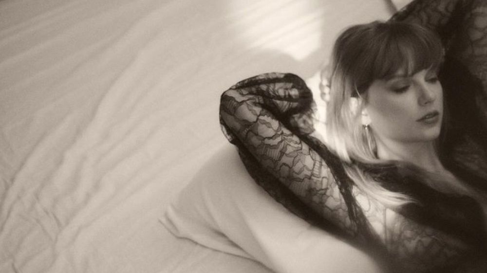 taylor swift for TTPD - a black and white photo of tayor swift laying back on a bed with her arms behind her head. Her eyes are closed.