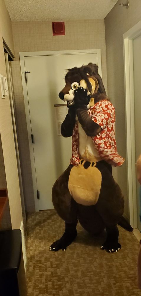 Otter fursuit gushing at himself in the mirror with hands on cheeks