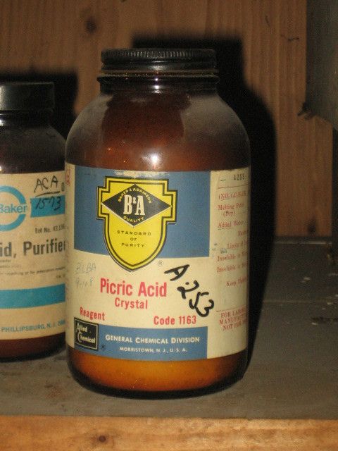 A jar of picric acid crystals, about as terrifying a substance as you will find on chemistry shelves.  It's on a dusty wooden shelving, with B&A brand name, in brown glass, and someone has written A-253 on it.