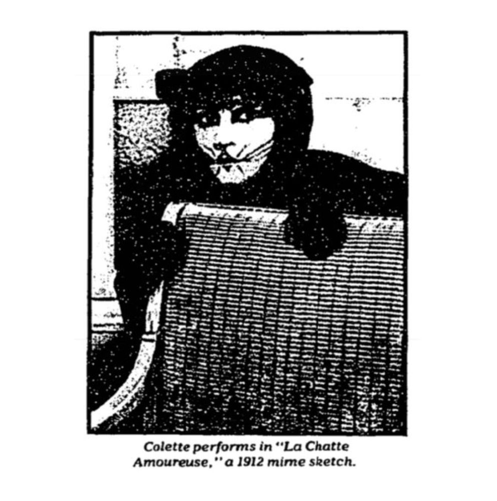 Black and white image of Colette performing "La Chatte Amoureuse," a 1912 mime sketch. Colette perches behind a chair, wearing a black cat costume with whiskers and stripes painted on her face.
