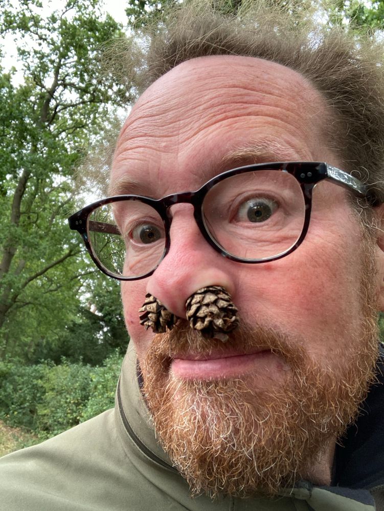 Man in glasses with two pine cones up his nose