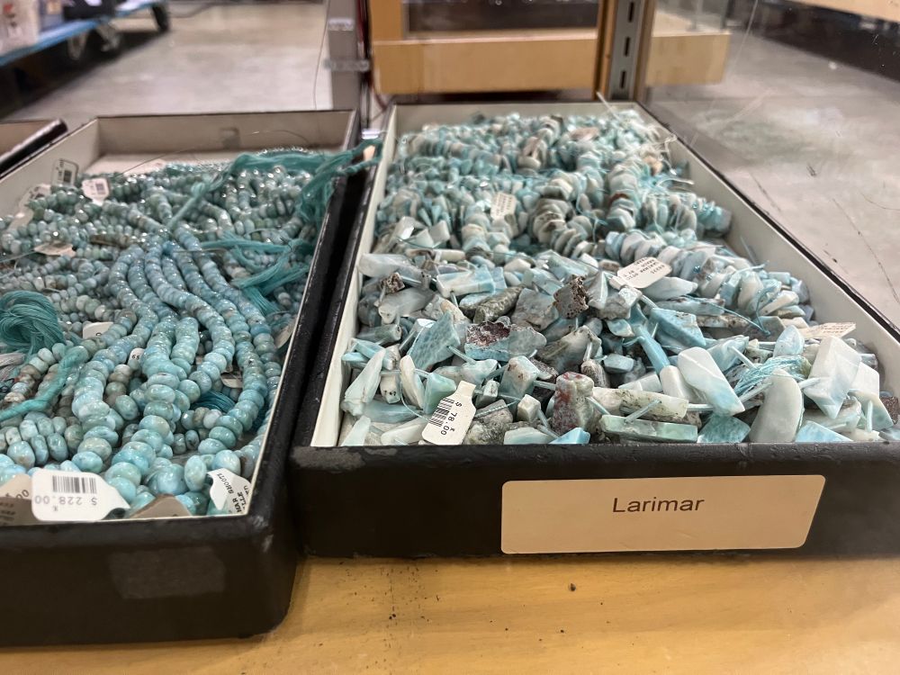 Box of raw pale blue larimar with polished beads in the adjacent box
