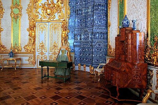 Catherine Palace in St Petersburg Russia. A room with very high ceilings and antique Russian furniture. The walls and doors are adorned with numerous gold embellishments.