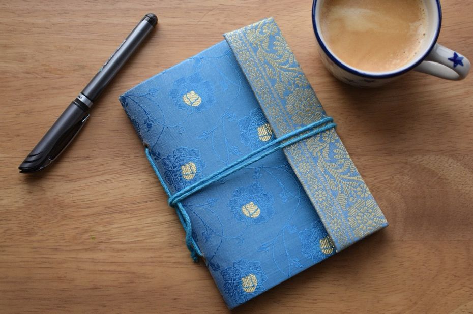 Notebook with blue sari cover on a table with cup of coffee and a pen