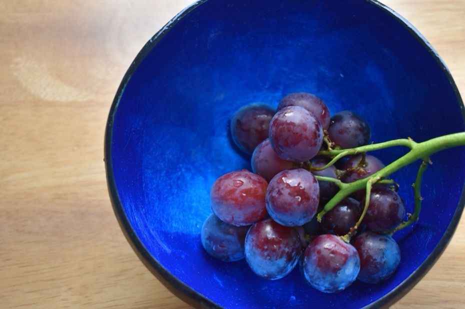 Shiny blue coconut bowl containing a bunch of red grapes 