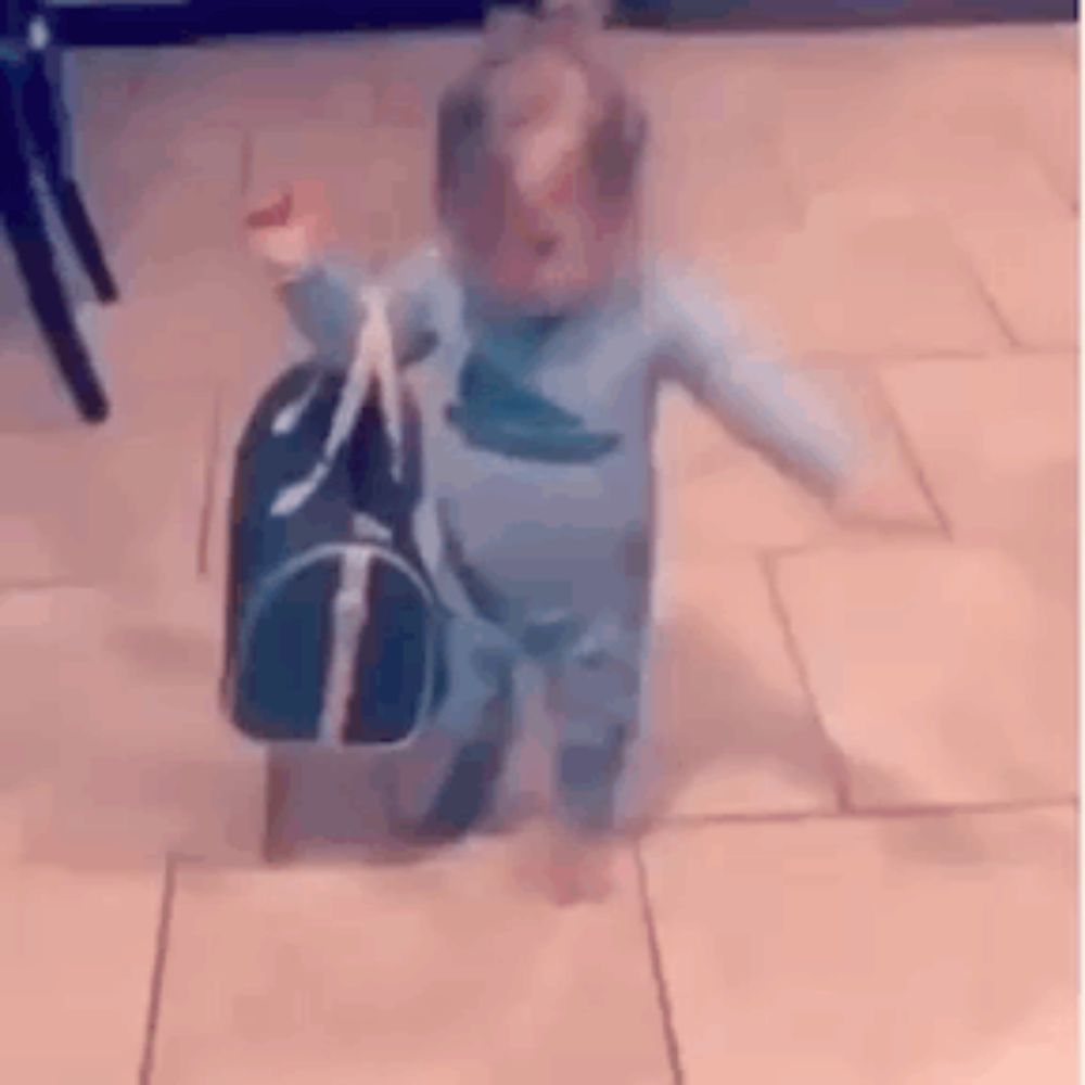 a baby is walking with a bag on the floor .