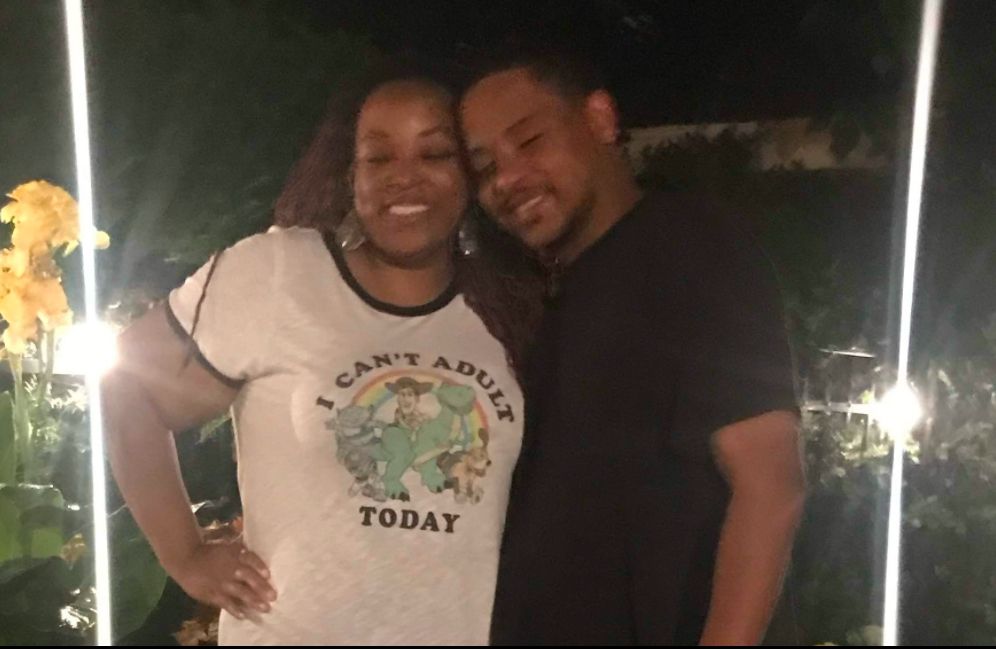 Woman smiling in white t shirt with cartoon characters that says “I can’t adult today” while hugging smiling man in black tshirt