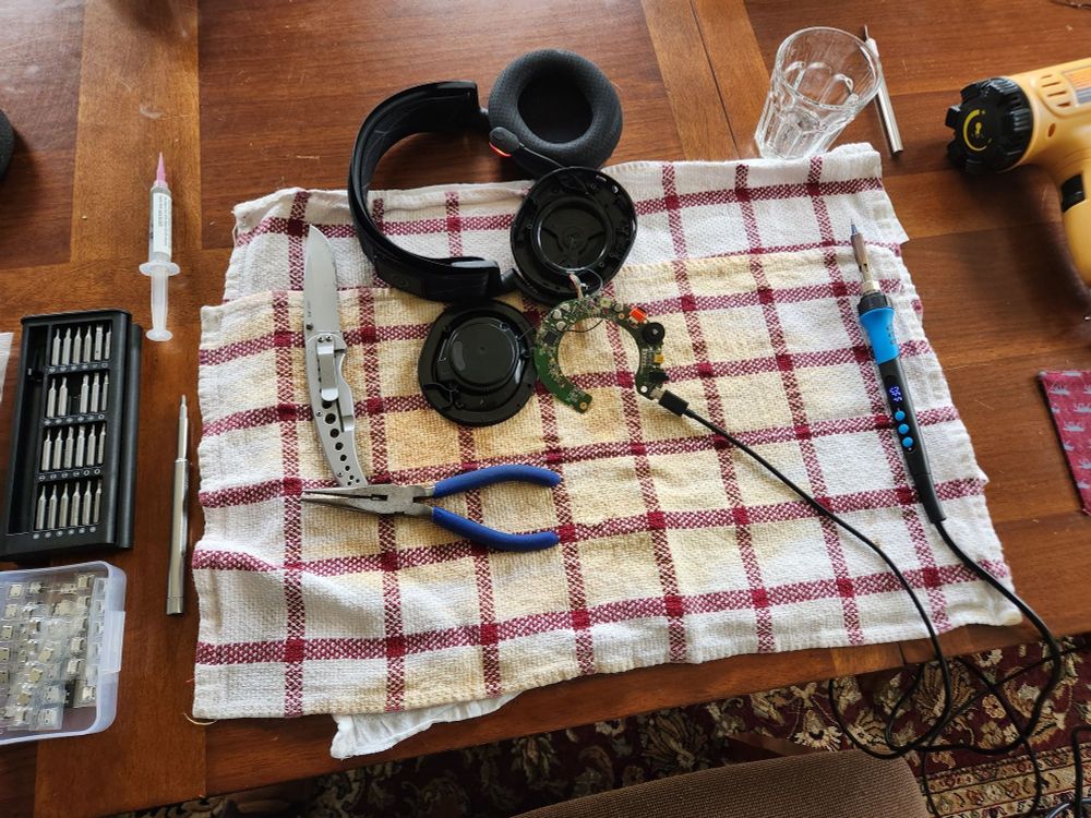 Picture of a wireless set of headphones that had been opened up with the circuit board exposed.  The headphones are connected to a charger to test that is working.