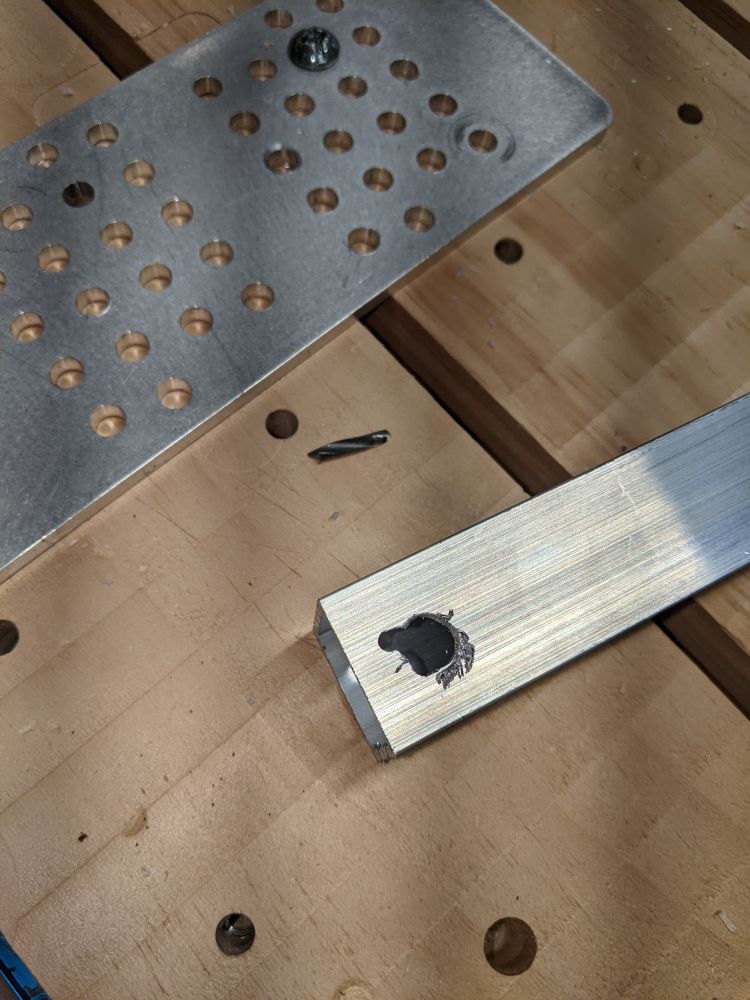 A CNC machine bed with a piece of aluminum tube. There's a hole in the tube with a ragged edge, where the workpiece slipped. And there's the tip of the broken bit laying next to it.