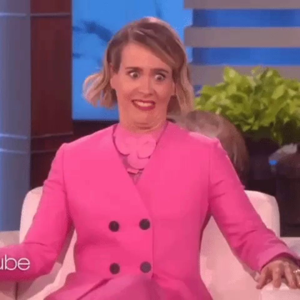 a woman in a pink jacket is making a funny face while sitting in a chair .