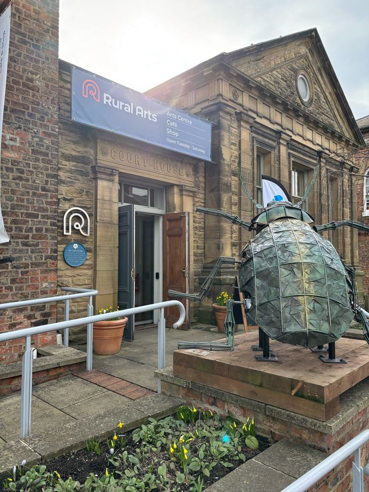 Giant beetle sculpture outside a grand looking building with a sign reading Rural Arts